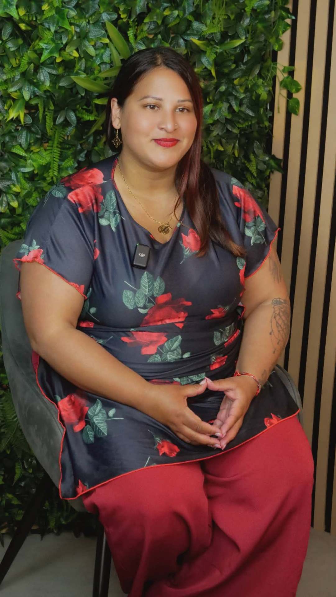 Katie Serenity en robe à fleurs, dans un fauteuil devant un mur végétal